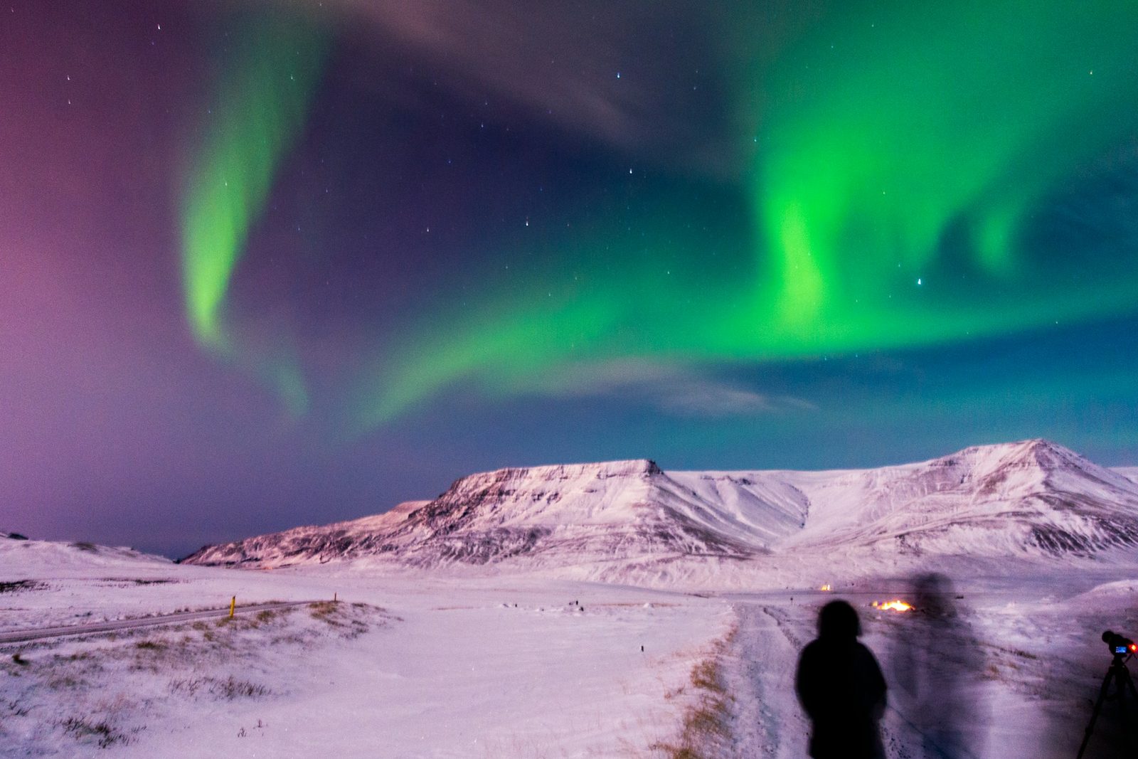 Una persona abrigada observa una aurora boreal sobre montañas nevadas en Islandia