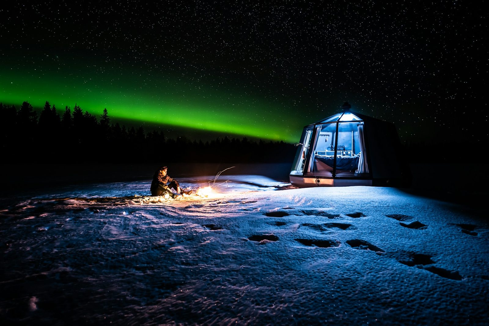 Iglú de vidrio iluminado en la nieve bajo una aurora boreal verde en Ranua, Finlandia