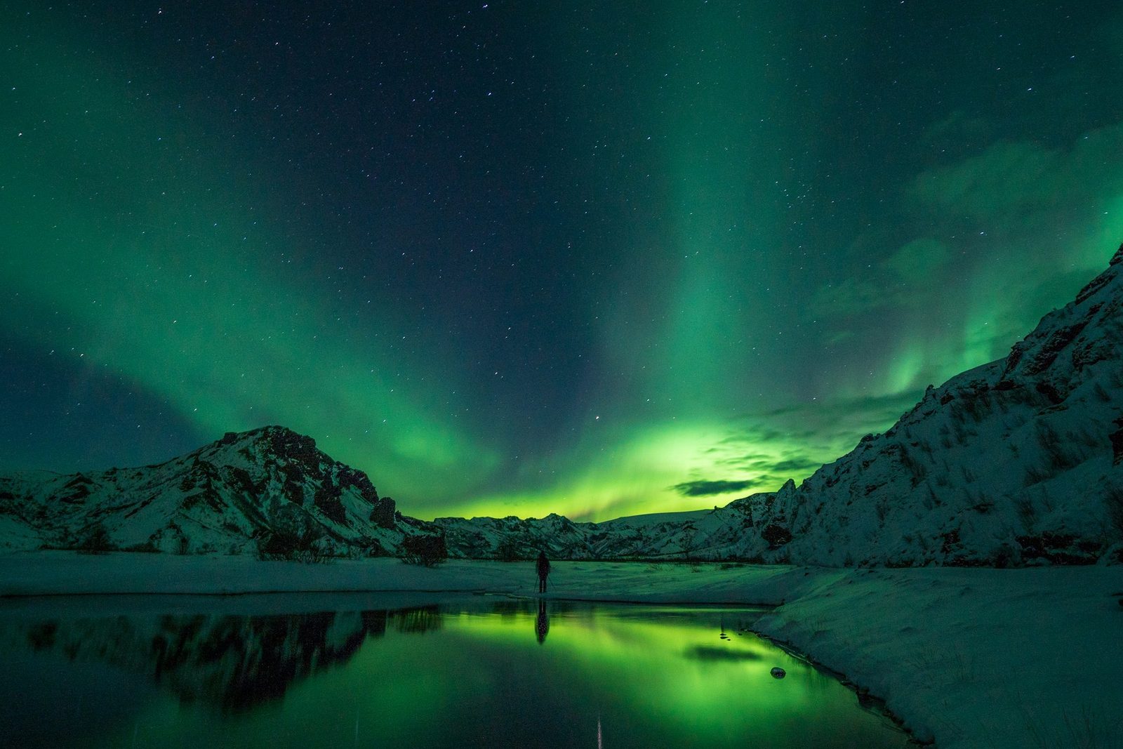 Aurora boreal verde reflejada en un río entre montañas nevadas de Islandia