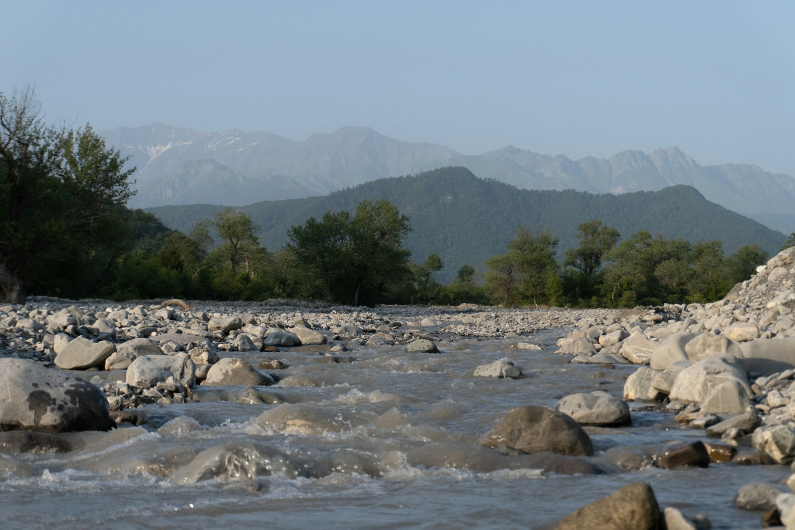 Río de piedras que baja entre árboles con montañas del Cáucaso al fondo