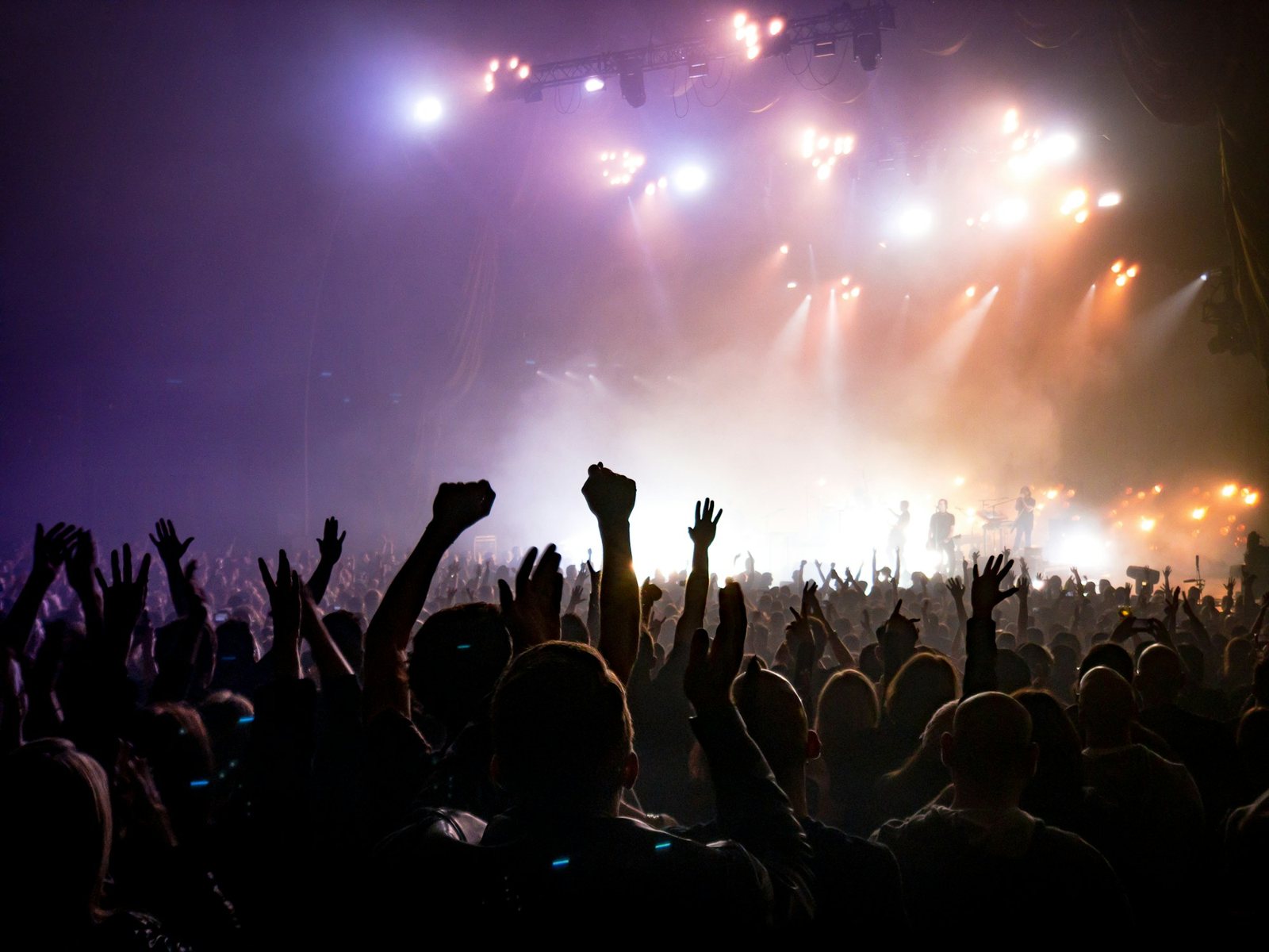 Público con las manos arriba frente a un escenario iluminado en un concierto