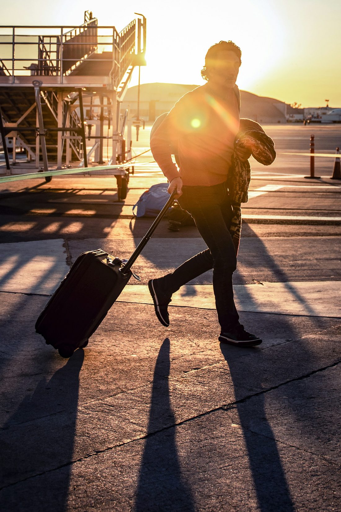 Viajero arrastrando una maleta de mano por la plataforma de un aeropuerto al atardecer