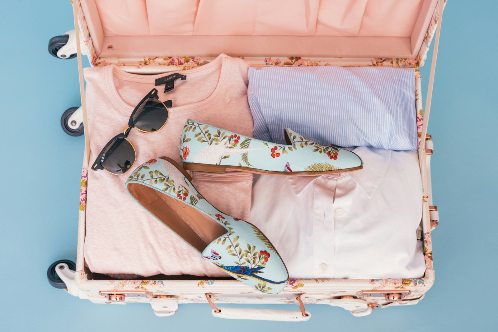 Maleta abierta con ropa, zapatos y gafas de sol