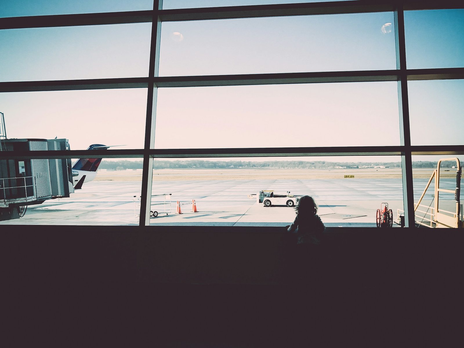 Niña mirando la pista por la ventana de un aeropuerto