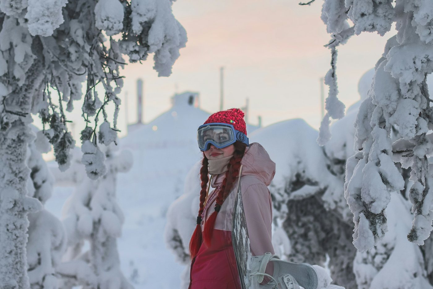 Viajera con chaqueta roja, gorro de lana y gafas de nieve entre árboles cubiertos de nieve