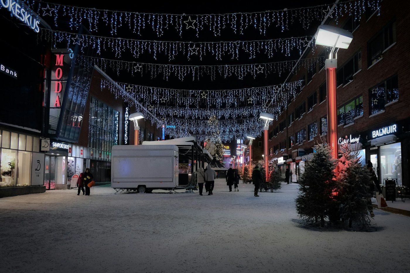 Calle peatonal de Rovaniemi cubierta de nieve con luces navideñas colgadas al anochecer