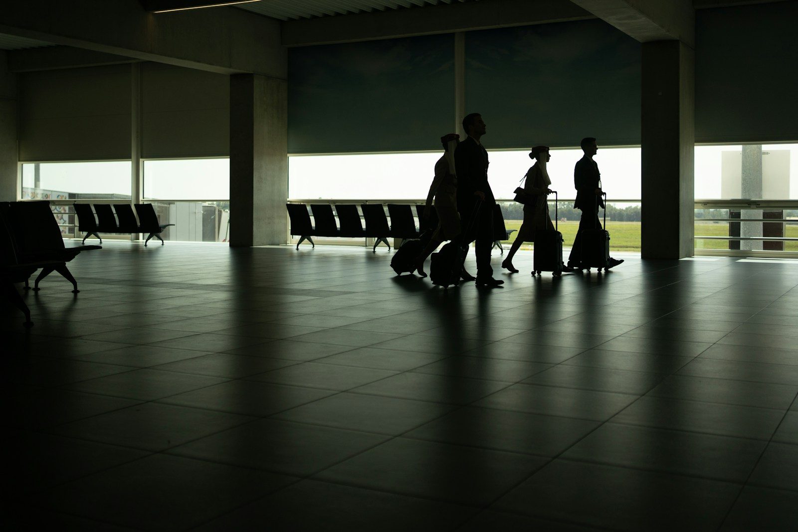 Siluetas de pasajeros y tripulación caminando por la sala de embarque de un aeropuerto