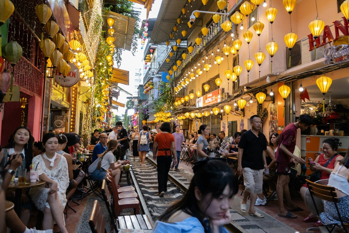 Calle angosta del centro de Hanói con vías de tren entre casas y viajeros caminando