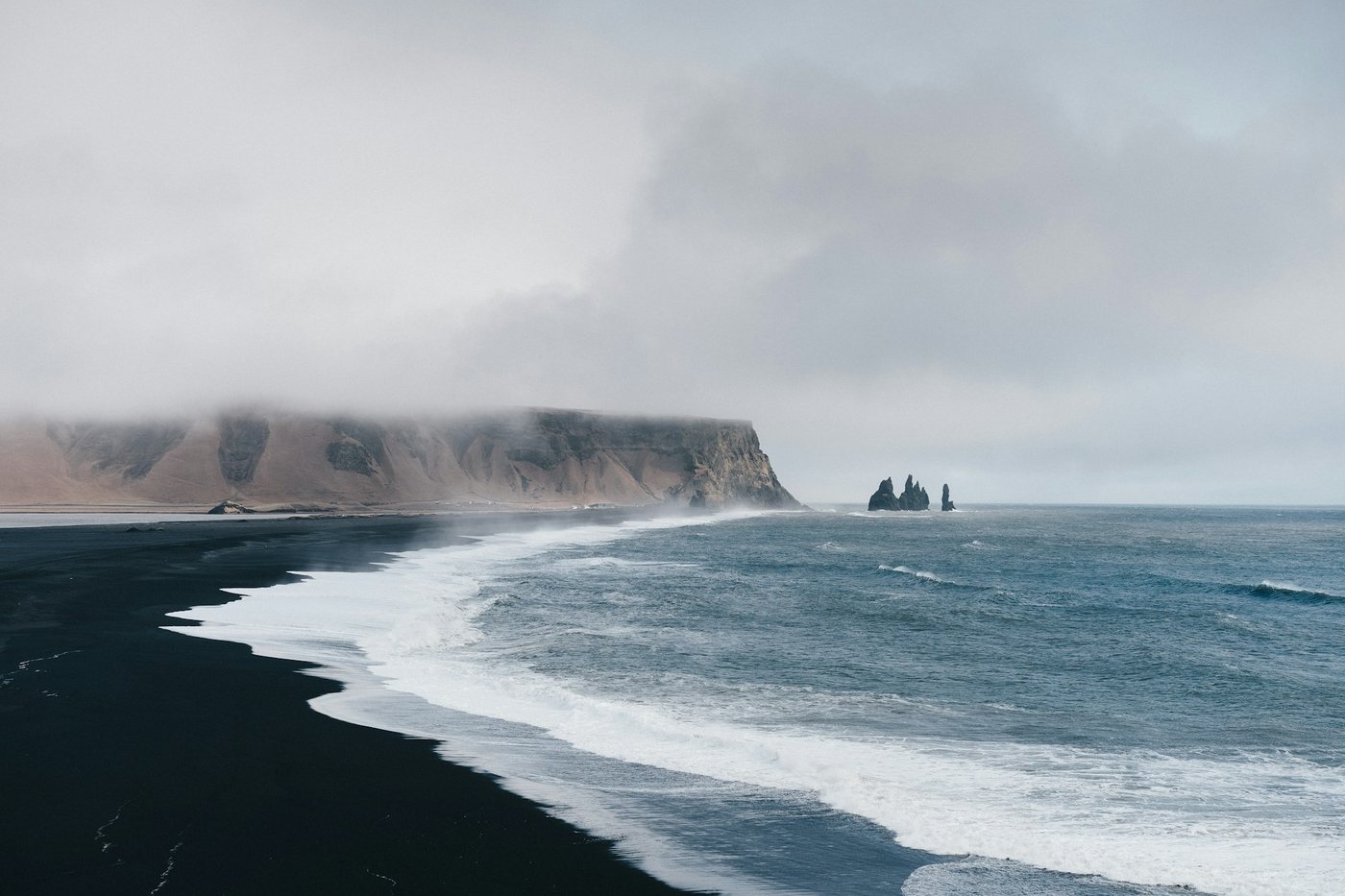 Olas sobre la playa de arena negra de Reynisfjara, cerca de Vík, con los farallones al fondo