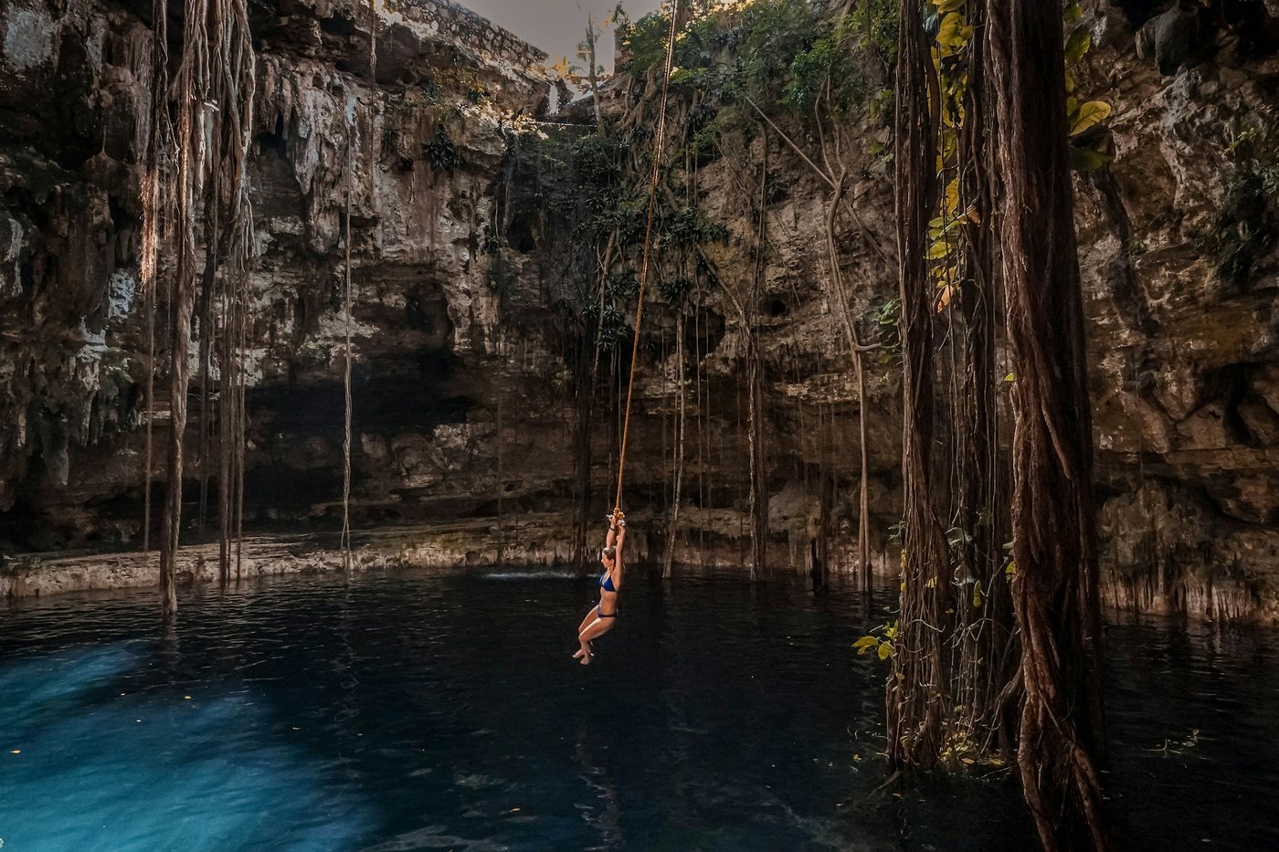 Cenote rodeado de raíces colgantes y paredes de roca, con una persona nadando