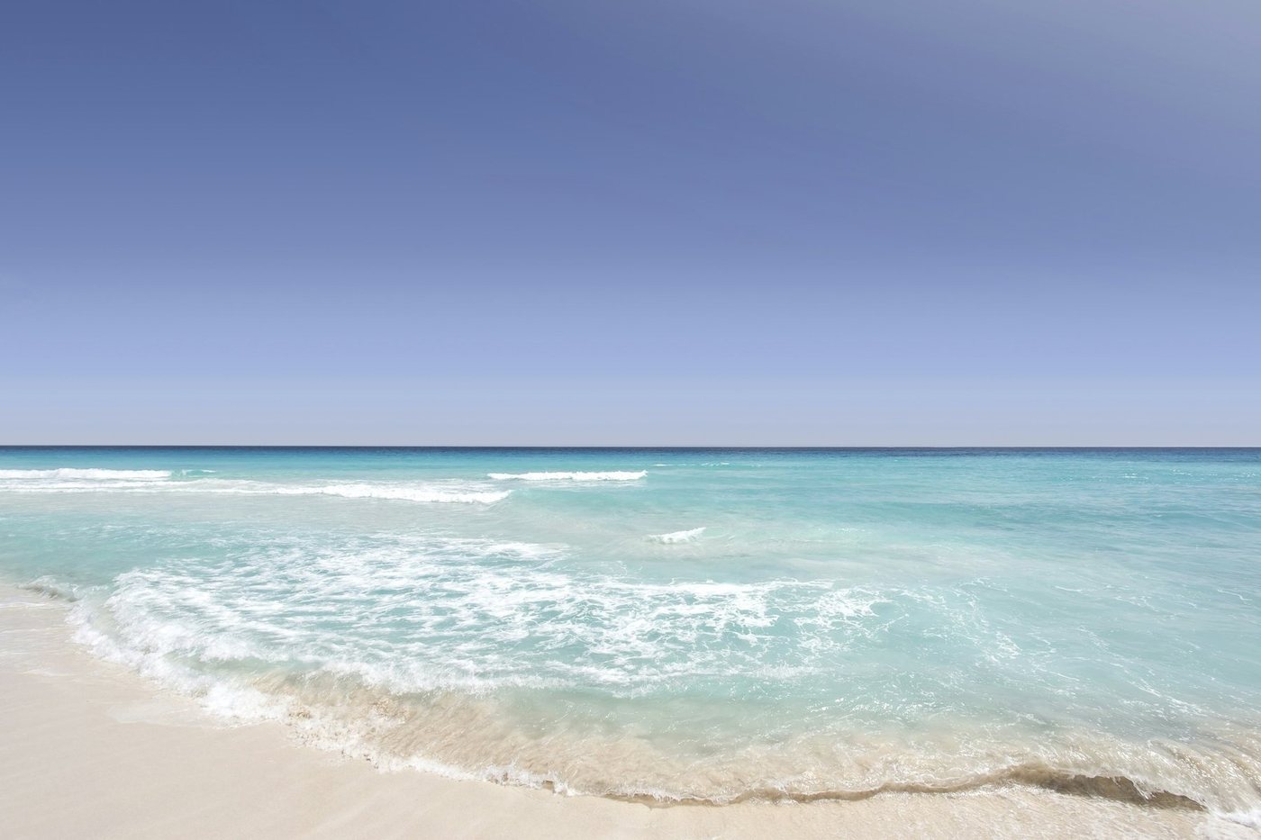 Ola suave sobre la arena blanca de una playa de Cancún con el mar turquesa al fondo
