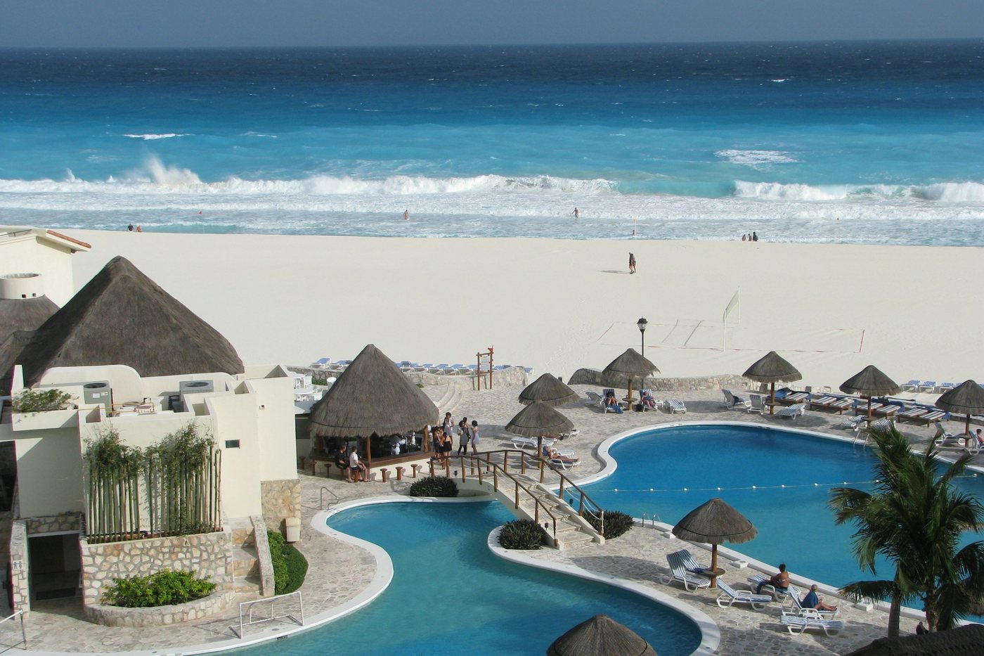 Piscinas de un hotel de Cancún con palapas y palmeras frente al mar