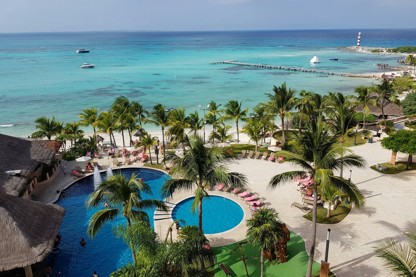 Jardines con palmeras y piscinas frente al mar turquesa en la Riviera Maya