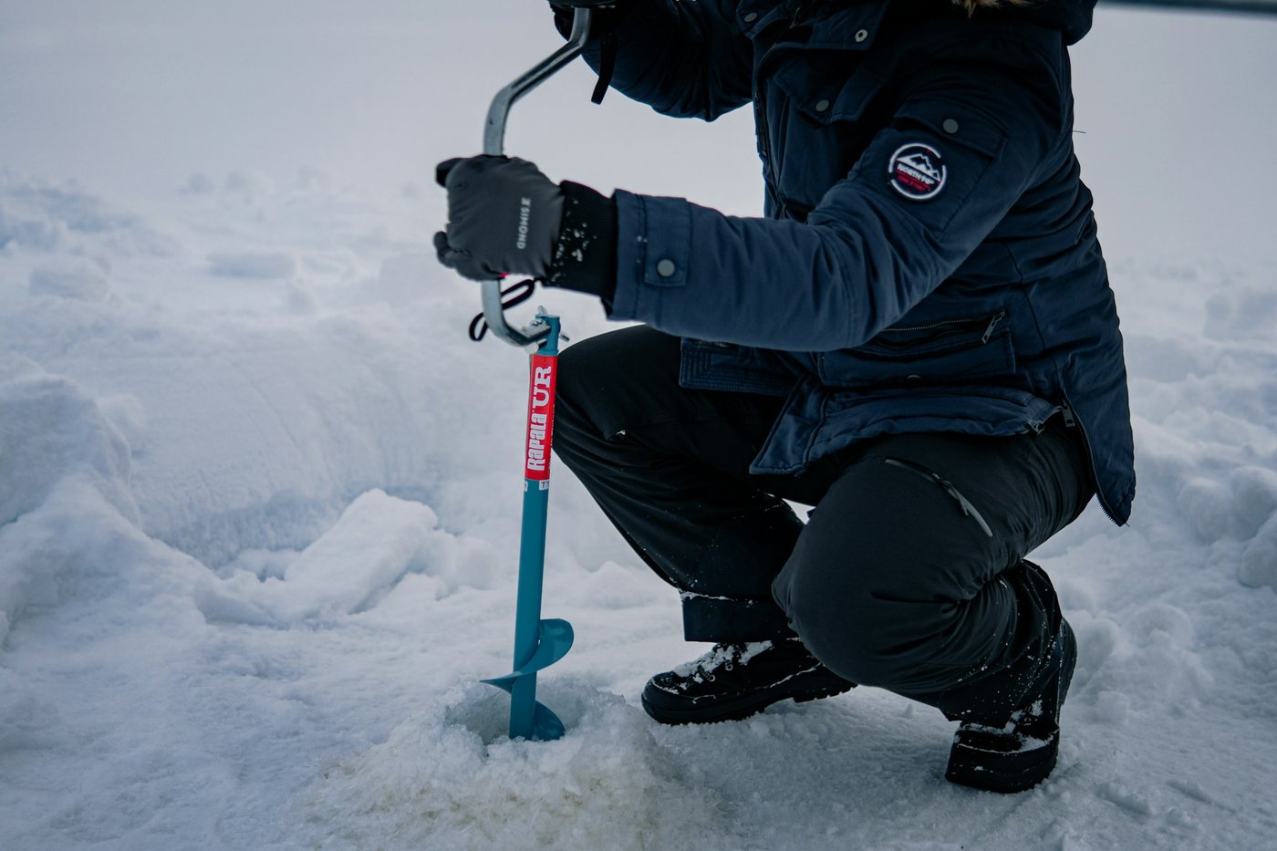 Viajero perforando el hielo de un lago congelado con un taladro manual