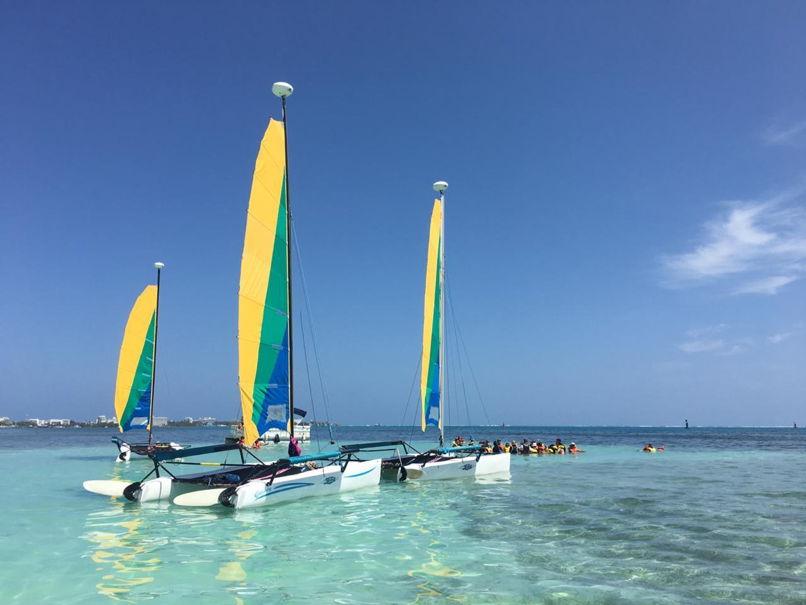 Catamaranes de vela amarilla fondeados sobre agua turquesa, con un grupo haciendo snorkel al fondo