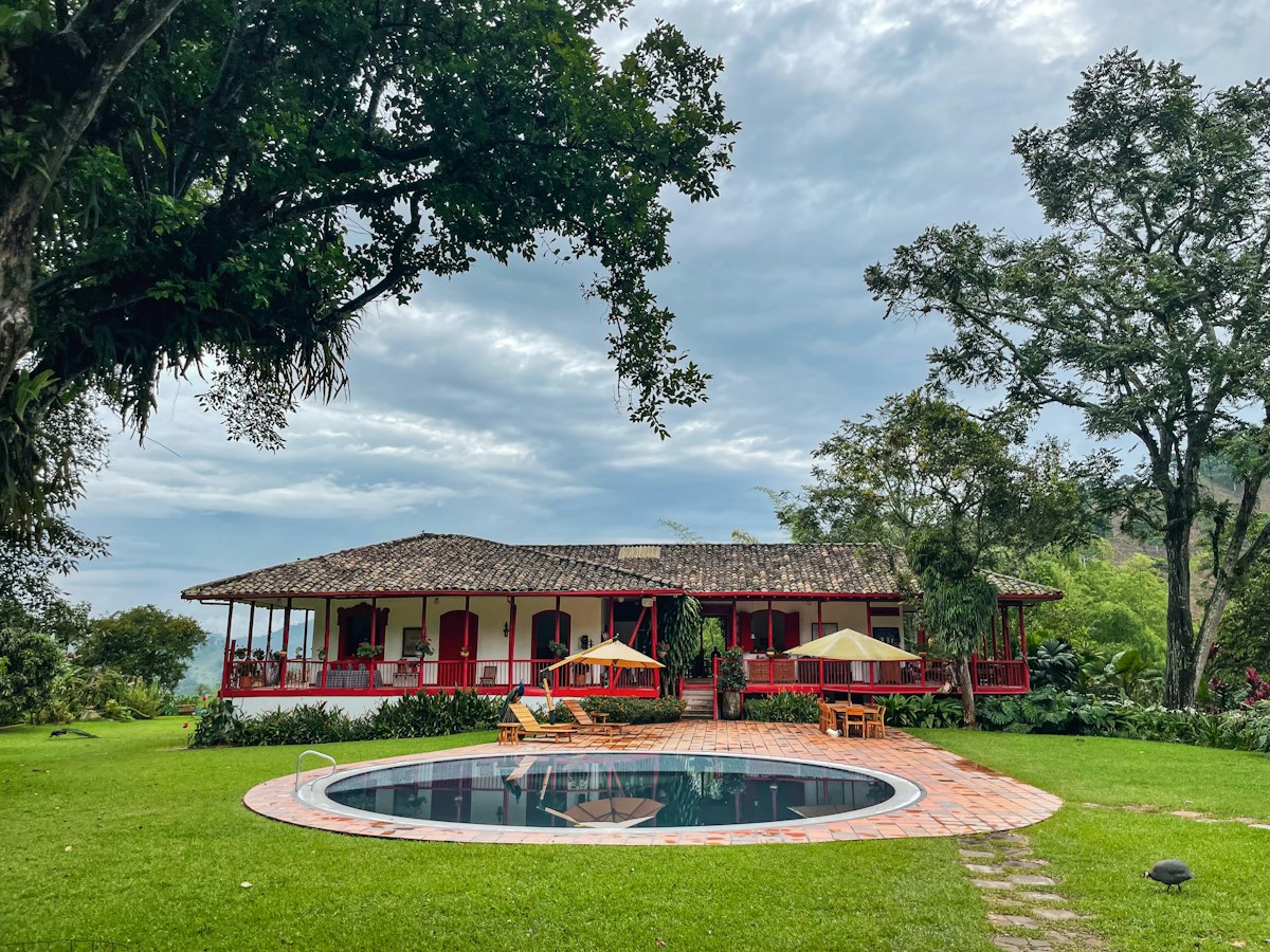 Casa de finca cafetera tradicional con corredores de madera y piscina rodeada de árboles